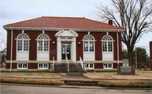red brick building with terra cotta roof, white framed windows and white columns stairs leading to entrance