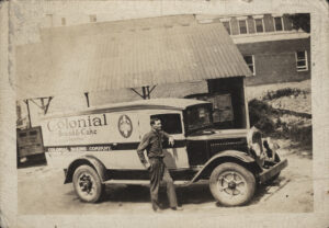 white man in work clothes standing next to truck with "colonial" on the side
