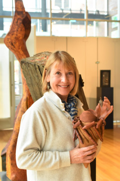 smiling blond woman holding artwork and standing in front of sculptures