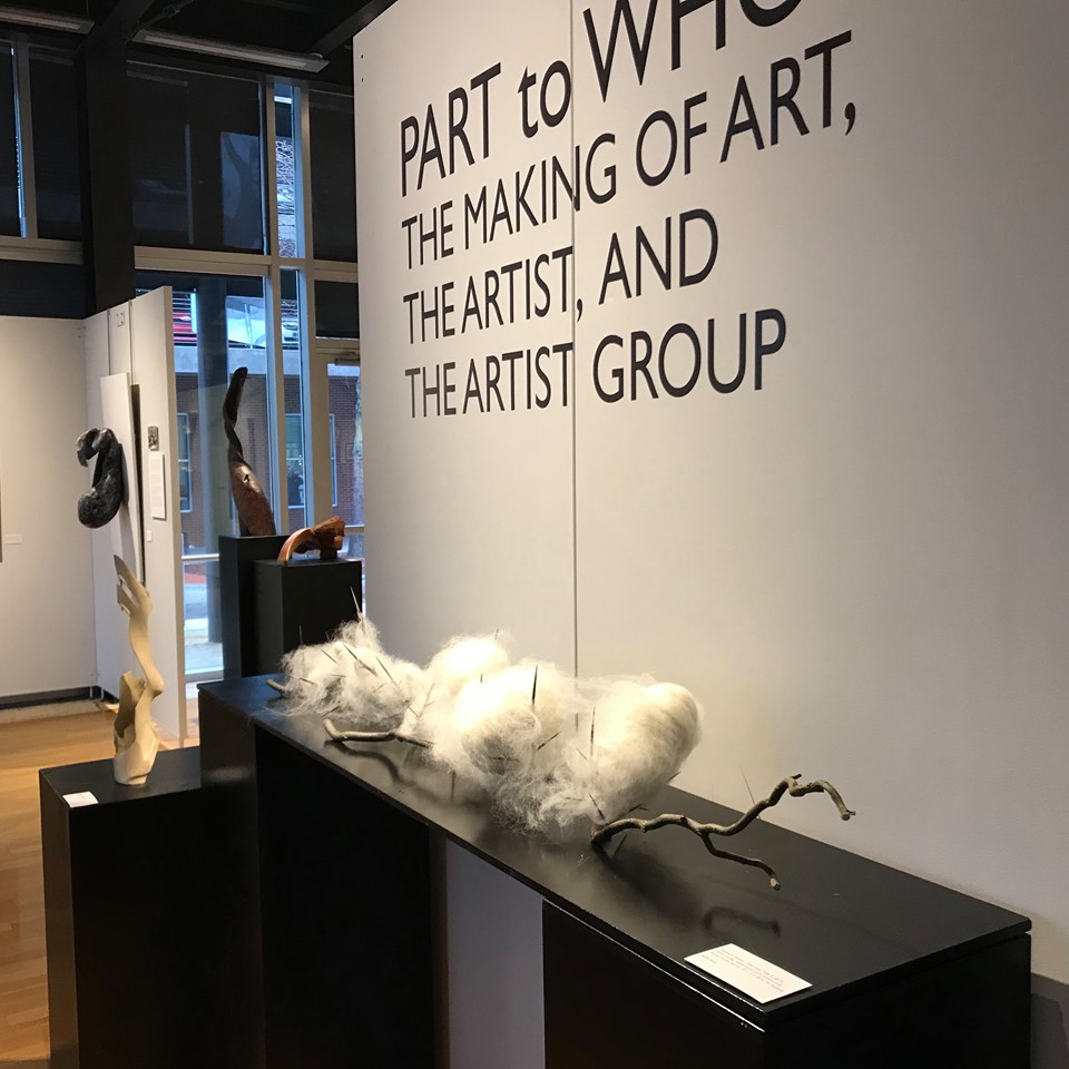 text on partition "part to whole the making of art the artist and the artist group" wtih black display table with white cotton on a branch