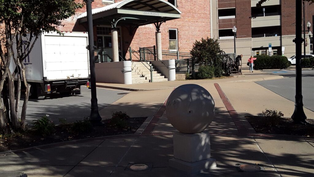 spherical sculpture on pedestal with building and truck in background