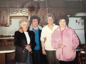 four older white women with short curly hair posing in a row