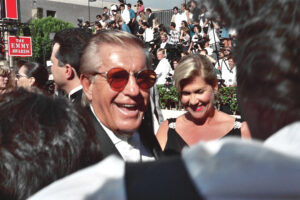 older man in sunglasses next to blond woman with crowd in background