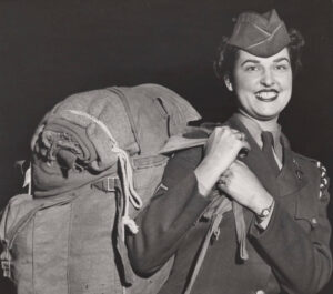 smiling white woman in military uniform with large pack on her back