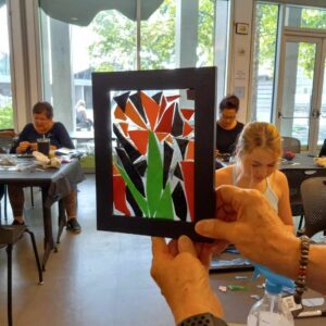 hands holding mosaic artwork with people at tables in the background