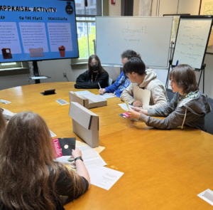 young people sitting at large wooden table looking at items from archival boxes