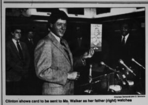 white man in suit in front of microphones holding a card in his left hand