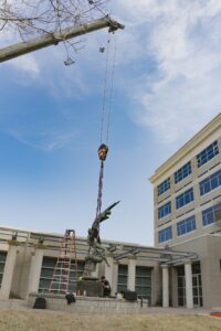crane lifting statue off base with building and sky in background