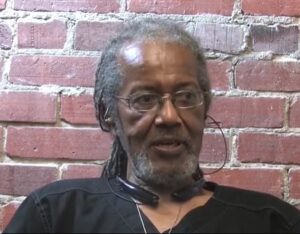 African American man with beard, glasses, black shirt and long dreadlocks in ponytail