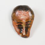 Man's visage and hair are painted on a stone or nut shell.