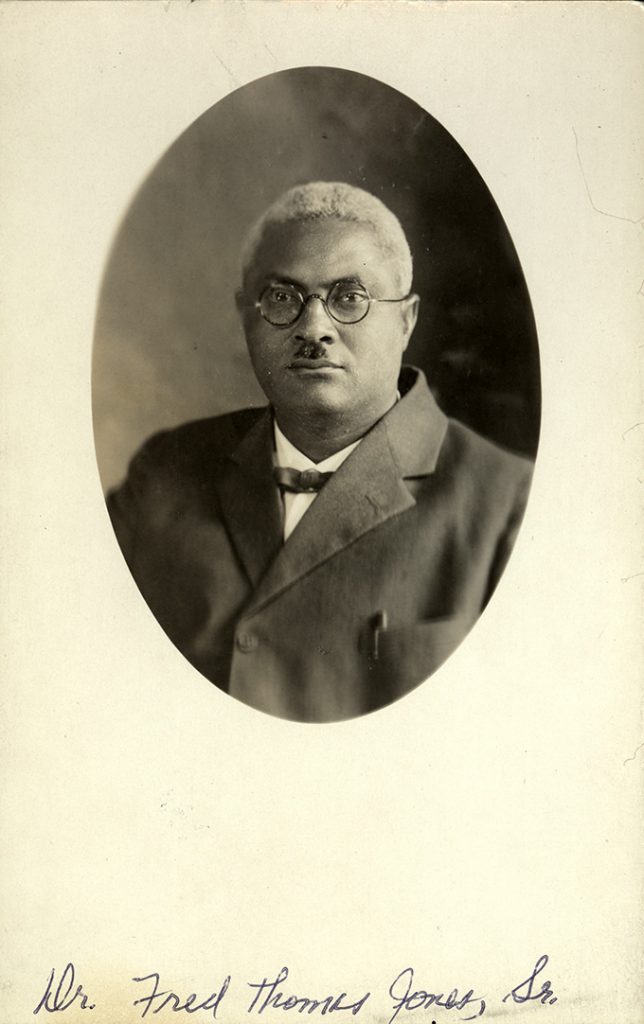 African-American man with mustache and glasses in suit in oval frame