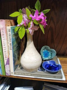 Vase with flowers books and heart shaped trays in bookshelf