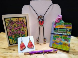 Multicolored floral greeting card butterfly wings earrings pen necklace and notebook on display