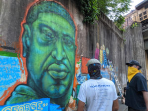 Artists wearing masks paint image of George Floyd on bridge wall.