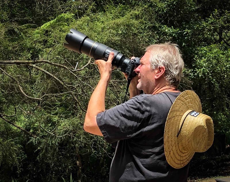 White man holding camera with long lens to his eye.