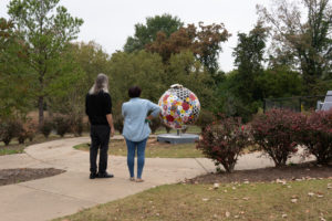 white man and black woman looking at large colorful globe artwork with trees and sidewalk surrounding it