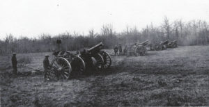 cannons with large wheels with men standing by them in large field