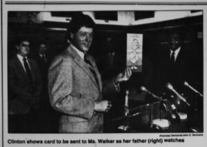 white man in suit in front of microphones holding a card in his left hand
