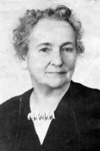middle-age woman with curly hair wearing black top and beaded necklace