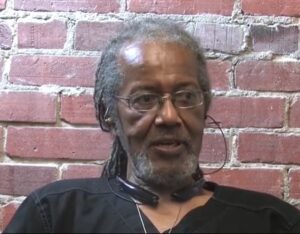 African American man with beard, glasses, black shirt and long dreadlocks in ponytail