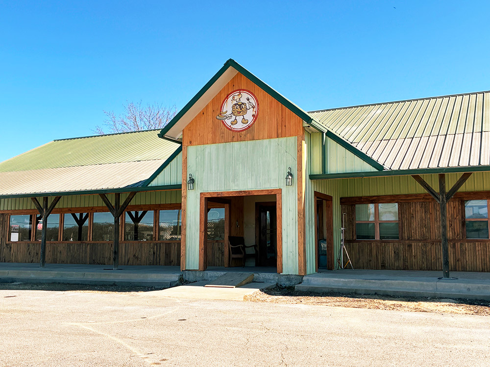 building with light green metal roof and windows along the front with waffle guy holding a pan and fork painted above entrance