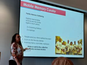 white woman with long brown hair standing next to screen with a slide saying Mobile Memory Curator