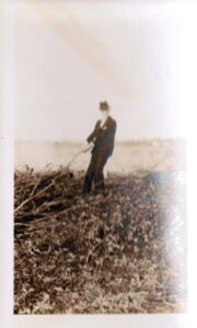 blurry photo of man in suit and hat in field pulling on a large branch