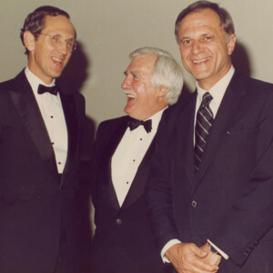 three white men in suits standing in a group and talking